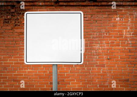 Blanker Wegweiser gegen die Ziegelwand. Leerer rechteckiger Rahmen für Text, Bilder und Werbung. Stockfoto