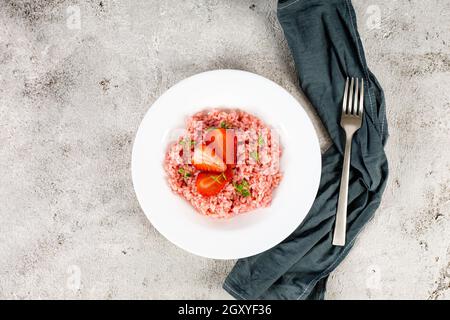 Risotto mit Erdbeerfrüchten serviert in einem weißen Gericht auf einem grauen Steintisch. Flach liegend mit Kopierraum. Italienische Gourmetküche. Selektiver Fokus. Stockfoto