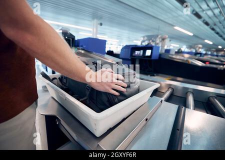 Sicherheitskontrolle am Flughafen. Junger Mann, der auf die Röntgenkontrolle seiner Tasche wartet. Stockfoto