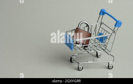 Metallschloss in einem Mini-Einkaufswagen auf grauem Hintergrund. Sicheres Online-Shopping-Konzept, Platz zum Kopieren Stockfoto