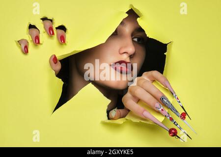 Porträt einer schönen Frau mit Kunst Make-up in glamourösen Stil, kreative lange Nägel auf einem gelben Hintergrund. Entwerfen Sie eine Maniküre. Beauty Face. Stockfoto