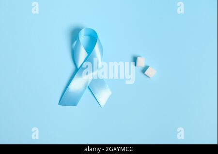 Flache Lay-Zusammensetzung aus reinen, raffinierten weißen Zuckerwürfeln und blauem Satinband, Symbol des Welt-Diabetes-Bewusstseins-Tages am 14. November. Isoliert über Colore Stockfoto