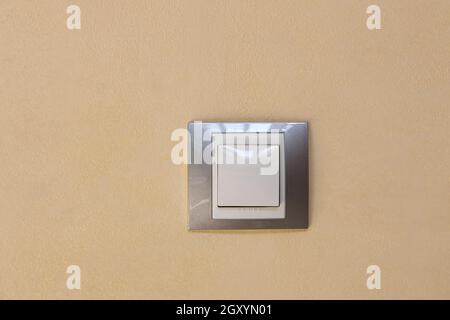 Modische, moderne weiße Lichtschalter in silbernem Rahmen an beigefarbener Strukturwand, gegenüberliegende Ansicht. Konzept Inneneinrichtung Details, elektrische Ausrüstung, Gerät. Stockfoto