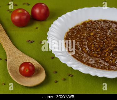 Hausgemachte Linsensuppe mit Schweinefleisch-Würstchen namens Chorizo und Blutwurst namens Morcilla in einem Gericht mit Tomaten und einem Löffel auf einer Tischdecke dekoriert Stockfoto