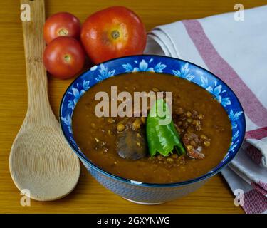 Hausgemachte Linsensuppe mit Schweinefleisch Würstchen genannt Chorizo, Blutwurst genannt Morcilla und grünem Pfeffer in einer Schüssel mit Tomaten, einem Löffel und dekoriert Stockfoto