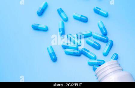 Blaue Kapsel Pillen aus der Flasche auf blauem Hintergrund verteilt. Pharmaindustrie. Arzneimittelentwicklung und neue Medikamentenforschung für die neue Behandlung Inf Stockfoto