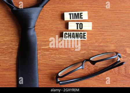 Draufsicht auf schwarze Krawatte, schwarze Gläser und Holzfliesen mit Text ZEIT ZU ÄNDERN Stockfoto