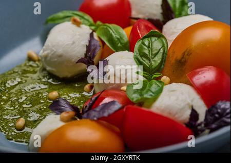 Traditioneller Caprese-Salat mit reifen Tomaten, Pinienkernen, Basilikum und Mozzarella-Käse in grauer Platte, selektiver Fokus Stockfoto