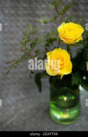 Schöne gelbe Rosen in einer grünen Vase stehen auf einer Decke. Überraschungs- und Urlaubskonzept. Nahaufnahme Stockfoto