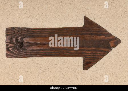 Klassische Pfeil aus dunklem Holz liegt im Sand. Mit Platz für Text. Ansicht von oben Stockfoto