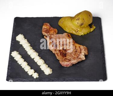 Beefsteak, Caliu-Kartoffeln und eine spanische Sauce mit dem Namen „all i oli“ oder „Aioli“ auf einem schwarzen Schieferbrett. Isoliert auf weißem Hintergrund Stockfoto