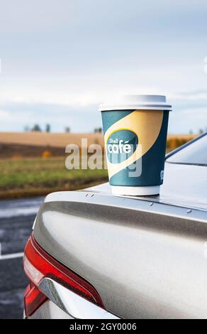 Kemerowo, Russland - 03. Oktober 2021: Shell Cafe to go Kaffeetasse steht auf der Autohaube. Pappbecher vom Shell Cafe zum Mitnehmen. Stockfoto