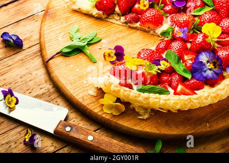 Erdbeerkuchen in Scheiben, verziert mit essbaren Blumen und Minze.Trendy Summer Berry Pie Stockfoto