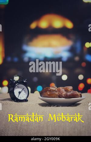 Konzept des Fastenmonats Ramadan. Selektives Fokusbild von Datteln, Obst und Wecker. Bokeh-Effekt Moschee im Hintergrund. Stockfoto