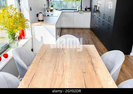 Ein modernes Esszimmer, das mit dem Wohnzimmer und der Küche verbunden ist, gibt es große Fenster in der Wand, einen sichtbaren Tisch und Stühle. Stockfoto