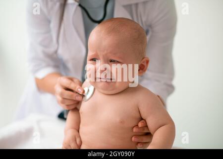 Weinender kleiner Patient, der sich der Brustauskultation unterziehen muss Stockfoto