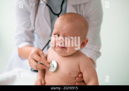 Trauriges Baby, das von einem Arzt mit einem Stethoskop untersucht wird Stockfoto