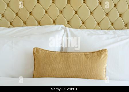 Gemütliches Bettenkonzept. Bettwäsche und Kissen mit gelben Motiven. Elegantes Schlafzimmer mit weißen Bettdecken und Laken. Weiche Kissen auf dem komfortablen Bett. Stockfoto