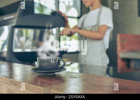 Der junge Besitzer des Cafés steht an der Theke. Der junge asiatische Barista lächelt und verwendet eine Kaffeemaschine an der Theke des Cafés, um Getränke zuzubereiten. Essen Stockfoto