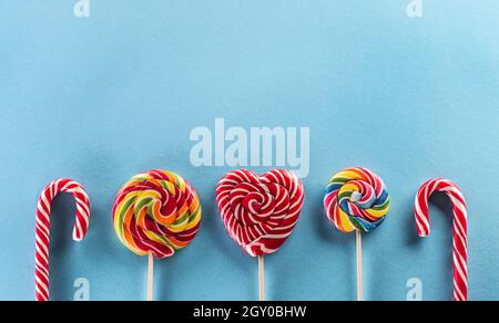 Eine bunte Linie von leckeren Regenbogenlutschern auf Holzstäben mit blauem Hintergrund. Stockfoto