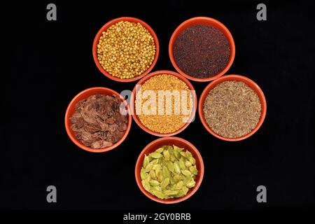 Draufsicht auf indische Gewürze, Fenugreek-Samen, Koriandersamen, Cardamom-Black, Cardamom-Green, Kreuzkümmelkerne, Senfkerne in Tonschüsseln auf schwarzem Hintergrund Stockfoto