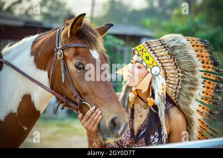 Pferd Nahaufnahme mit schönen böhmischen Mädchen und Schönheit rot braunen Pferd. Injun Frau im Krieg Haube Schönheit Porträt Native American Feder Chef Kopfschmuck Stockfoto