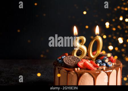 Schokoladengeburtstorte mit Beeren, Keksen und achtzig goldenen Kerzen auf schwarzem Hintergrund, Kopierraum Stockfoto