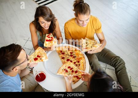 Zeit mit Freunden verbringen. Gruppe von fröhlichen jungen Menschen reden und essen Pizza zusammen Stockfoto