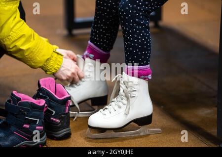 Frau hilft, ihre Tochter ihren Abbildung legen Skates auf, bevor Sie sie zu einer skating Lektion. Stockfoto