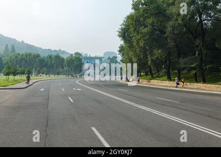 Pjöngjang, Nordkorea - 28. Juli 2014: Eine leere Straße auf einer Straße in Pjöngjang. Eine Tafel mit den nordkoreanischen Führern Kim Il Sung und Kim Jong Il ON Stockfoto