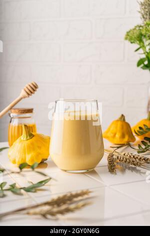 Ein natürlicher Smoothie aus gelbem Kürbis. Herbstgetränk mit Honig und Milch. Auf hellem Hintergrund, senkrechte Position Stockfoto
