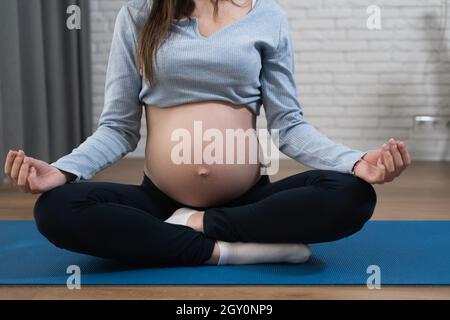 Bauch einer Schwangeren, sitzt sie auf dem Boden in der Lotusposition. Meditation für werdende Mütter. Stockfoto