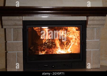 Kamin im Inneren. Das Feuerholz brennt mit einer roten Flamme. Wohnkomfort und Urlaubskonzept. Stockfoto