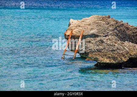Verrostete alte Leiter im Meer, die auf einem Stein gelehnt ist Stockfoto