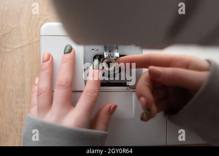 Die Näherin ersetzt die Spule in der Nähmaschine, Nahaufnahme der weiblichen Hände mit Maniküre. Small Business-Konzept. Stockfoto