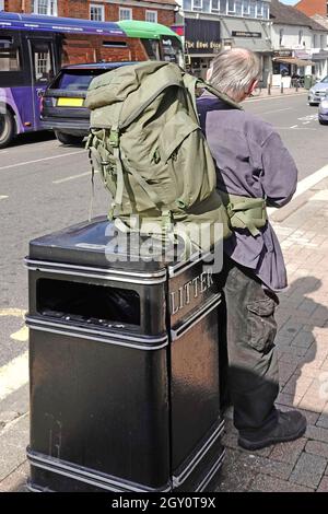 Straßenszene im Stadtzentrum grauhaariger Mann, der einen großen schweren Rucksack auf dem Abfalleimer für Straßenmöbel ruht, um ihm das Gewicht von den Füßen zu nehmen England Großbritannien Stockfoto