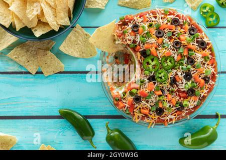Blick von oben auf ein hausgemachtes mexikanisches Dip mit mehreren Schichten, serviert mit einer Schüssel Nacho-Chips. Stockfoto