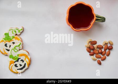 Halloween kreativer Hintergrund: Kürbisbecher und hausgemachte Kekse in Form von niedlichen Kürbissen und Mandeln Herz. Trick or Treat-Konzept. Ästhetischer Herbst Stockfoto