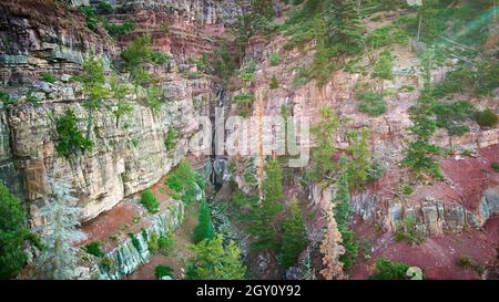 Großer Canyon mit einem hohen Wasserfall, der von oben nach unten fließt, und Bäumen, die auf Felsen wachsen Stockfoto