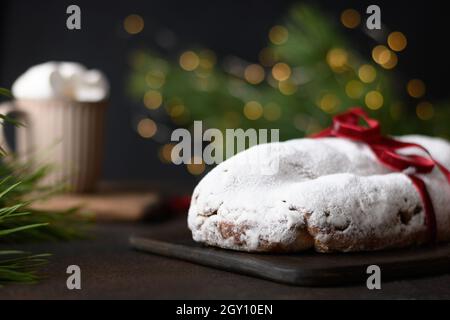 Weihnachts-Stollen und Kaffeetasse mit Moormarmelow, immergrünen Ästen und Girlande auf einem braunen Tisch. Nahaufnahme. Stockfoto