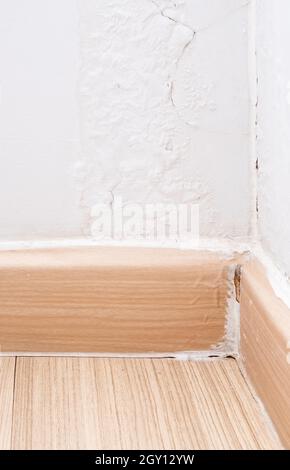 Nahaufnahme der zerbrochenen Fußböden an der Ecke des Wohnzimmers, die Farbe an der Wand hat sich aufgrund der Feuchtigkeit aus dem Regen abgeblättert. Vorderansicht Stockfoto
