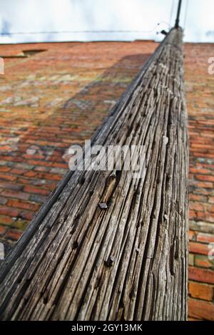 Rauer strukturierter hölzerner Telefonmast, der ein rotes Ziegelgebäude hochführt Stockfoto