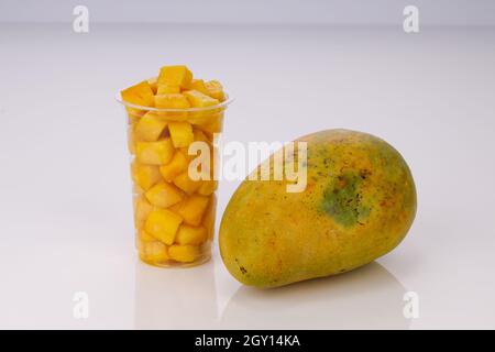 Reife Mango Würfel oder geschnittenes Stück in einem transparenten Glas mit Mango in der Nähe auf weißem Hintergrund angeordnet. Stockfoto