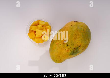 Reife Mango Würfel oder geschnittenes Stück in einem transparenten Glas mit Mango in der Nähe auf weißem Hintergrund angeordnet. Stockfoto