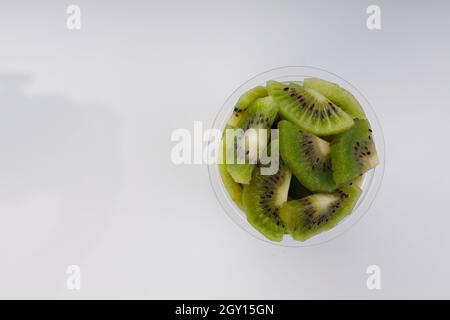 Kiwi-Fruchtscheiben oder -Stücke, die in einem transparenten Glas mit weißem Hintergrund angeordnet sind. Stockfoto