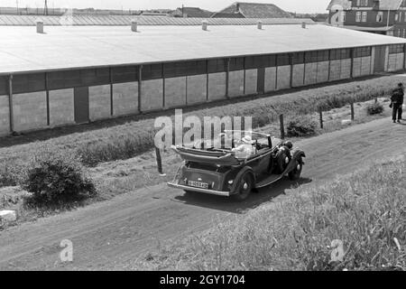 Unterwegs in einem Audi Cabrio zu den Garagen in Norddeich, Deutschland 1930er Jahre. Menschen in einem Audi Cabrio zu den Garagen bei Norddeich, Deutschland 1930. Stockfoto