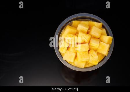 Ananaswürfel in transparentem Glas mit schwarzem Hintergrund angeordnet Stockfoto