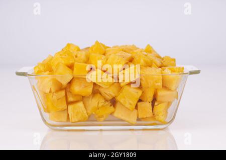 Ananaswürfel in quadratischem Behälter aus transparentem Glas mit weißem Hintergrund angeordnet Stockfoto