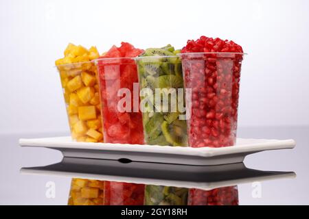 Wassermelone, Ananas, Granatapfel und Kiwi-Scheiben in transparenten Gläsern mit weißem Hintergrund, isoliert Stockfoto