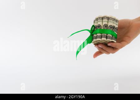 Weibliche Hand hält rollte 100-Dollar-Scheine mit grünem Geschenkband gebunden. Stockfoto